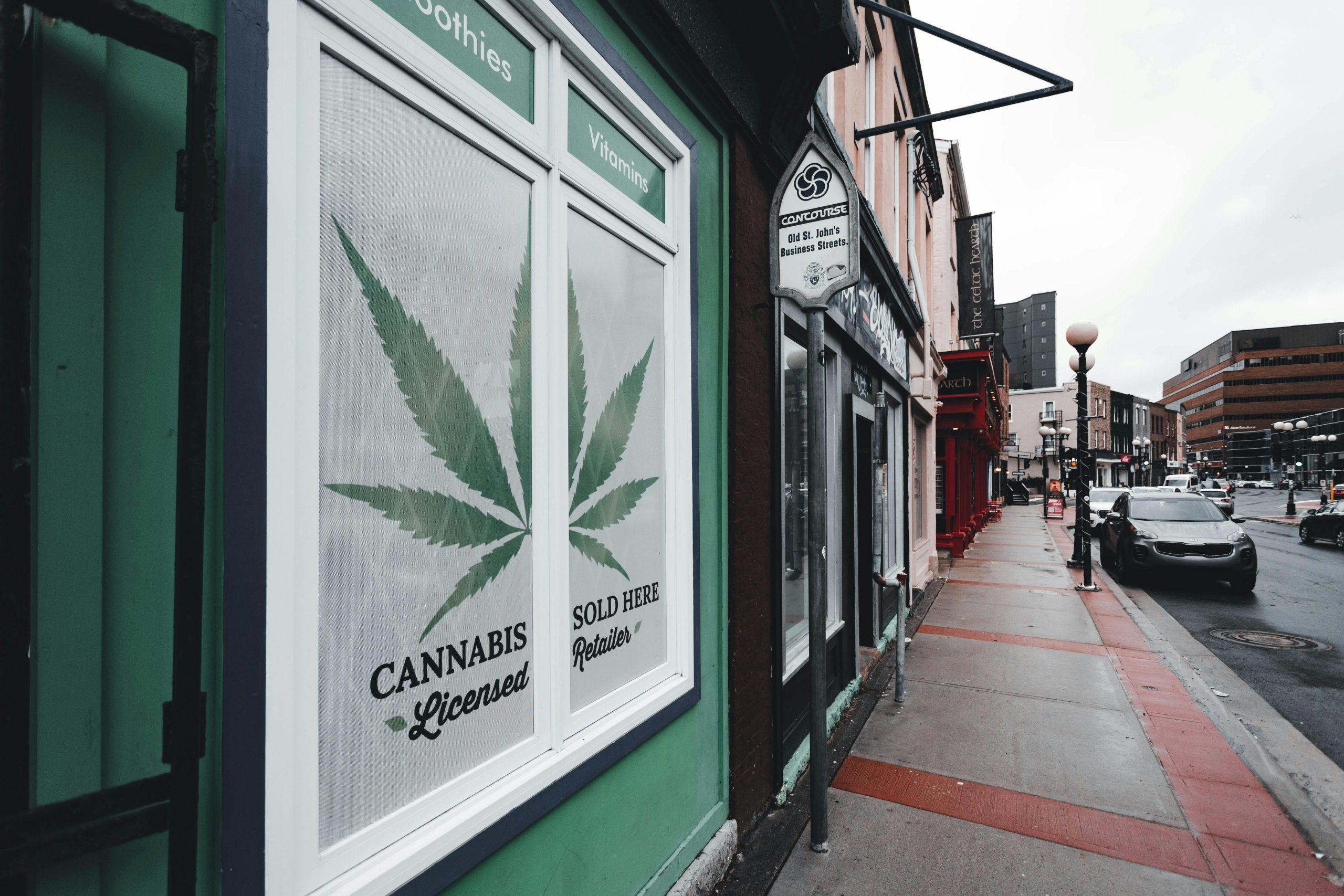Street view of licensed cannabis retailer sign in urban setting with storefronts and cars.