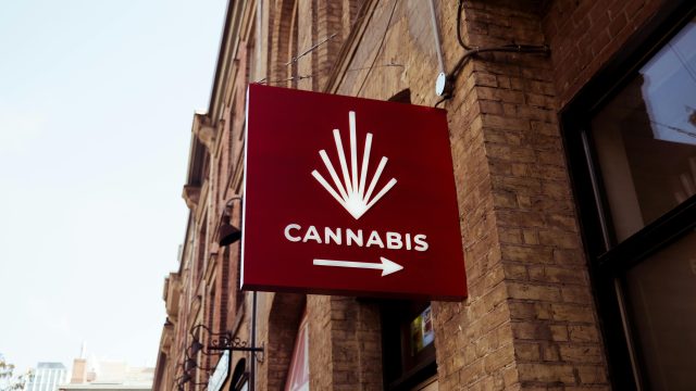 A red sign featuring a cannabis emblem on a city building facade, indicating a store direction.
