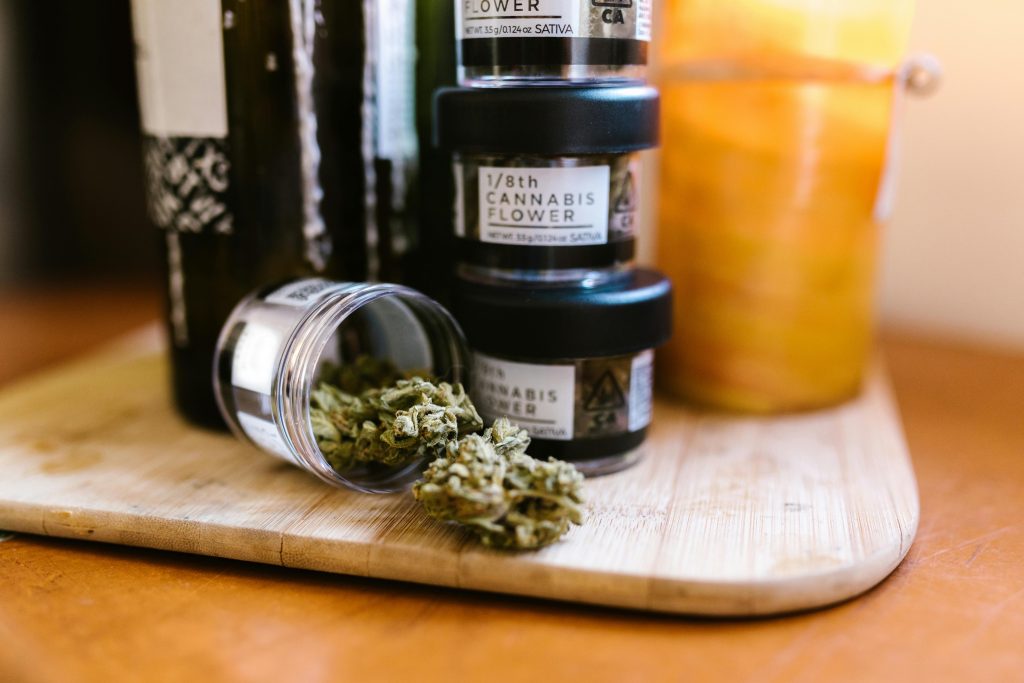 Cannabis buds in glass jars on a wooden board indoors with soft lighting.
