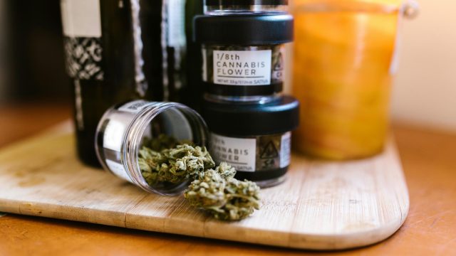 Cannabis buds in glass jars on a wooden board indoors with soft lighting.